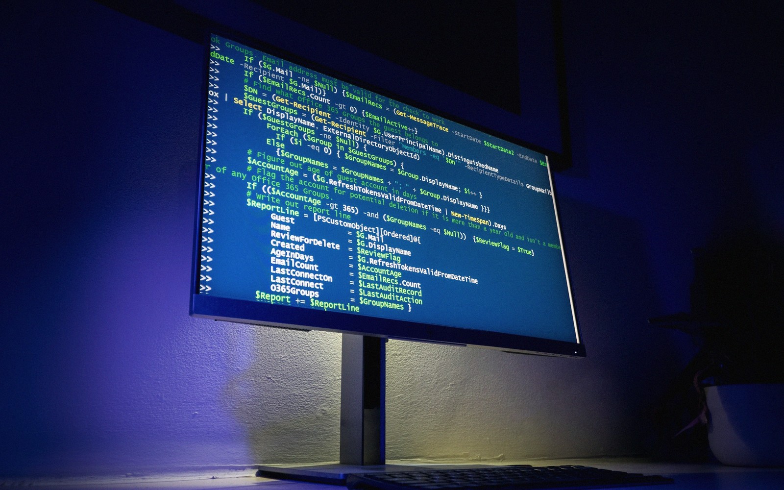 Computer monitor displaying colorful lines of PowerShell code in a dark room
